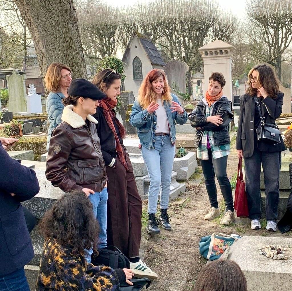 A group of young women listen intently to a speaker in a historic cemetery.
