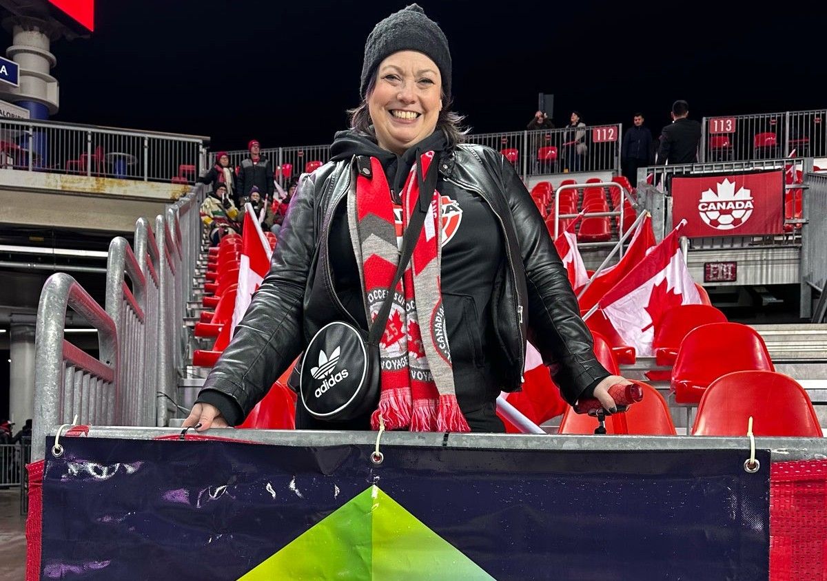 Smiling woman in black jacket and red-and-white scarf at a night stadium game.
