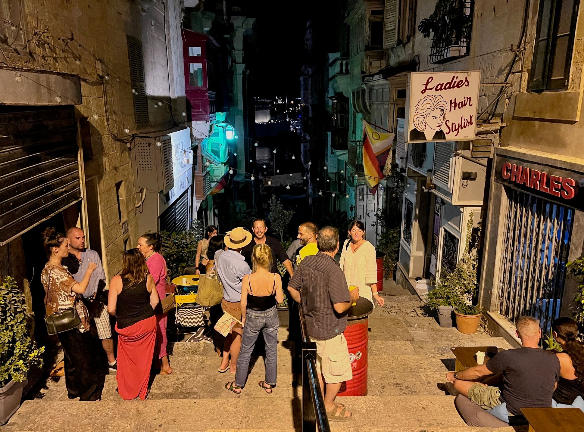 People gather in a narrow, dimly lit alleyway at night with buildings and a toilet sign.