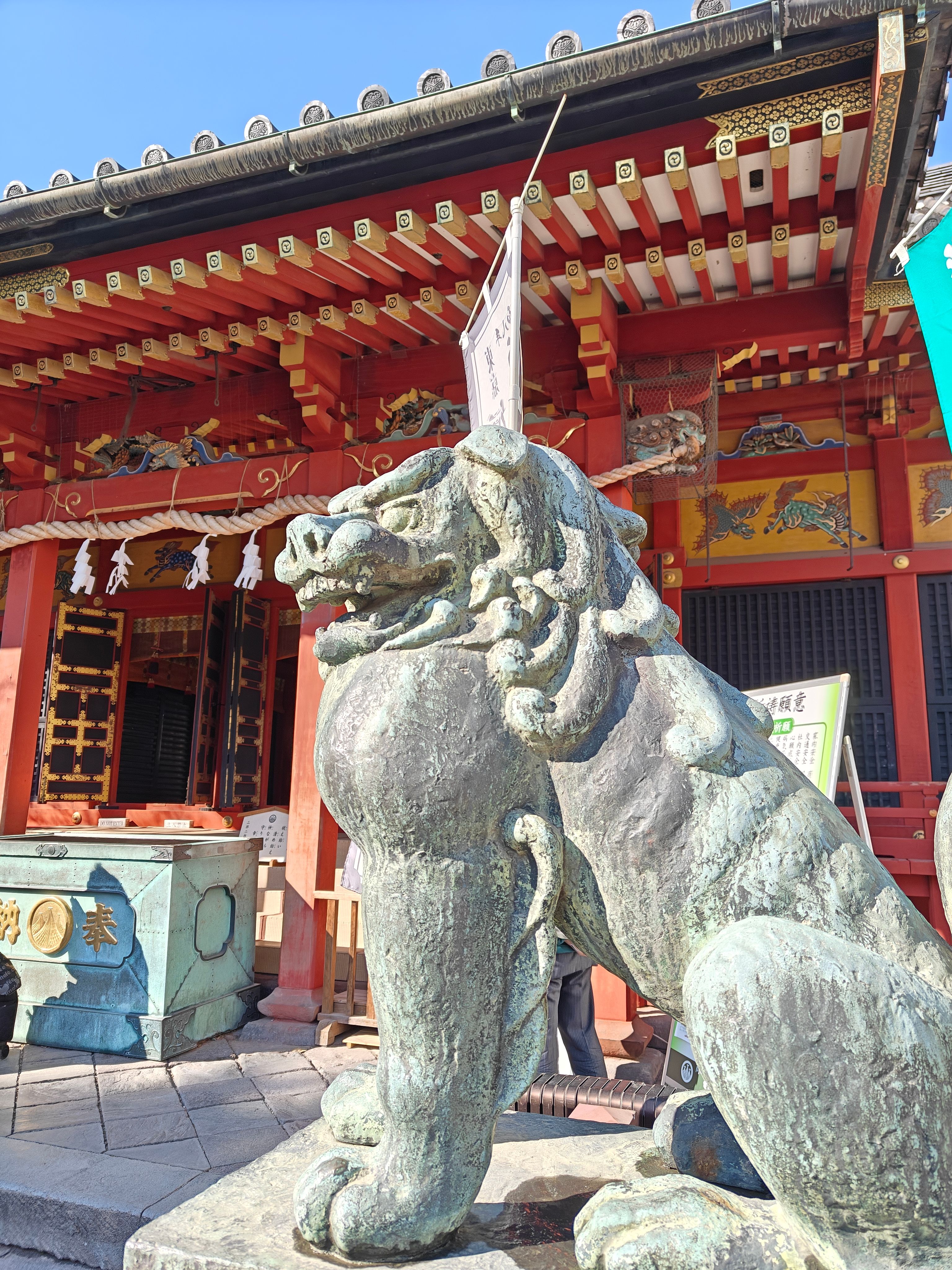 Bronze guardian lions stand before a vibrant red Japanese shrine with ornate carvings.