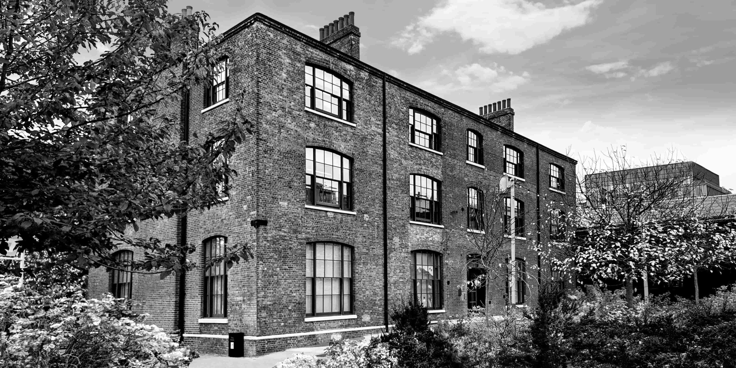 Historic brick building with many windows and prominent chimneys, surrounded by trees.