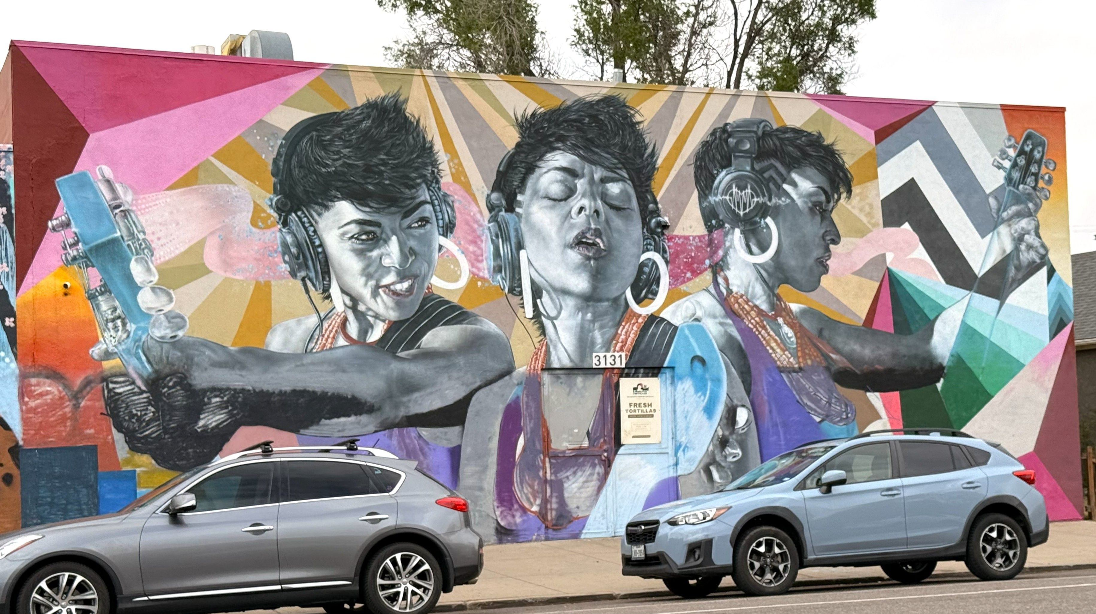 A vibrant mural depicts three women's faces in grayscale against colorful geometric patterns.