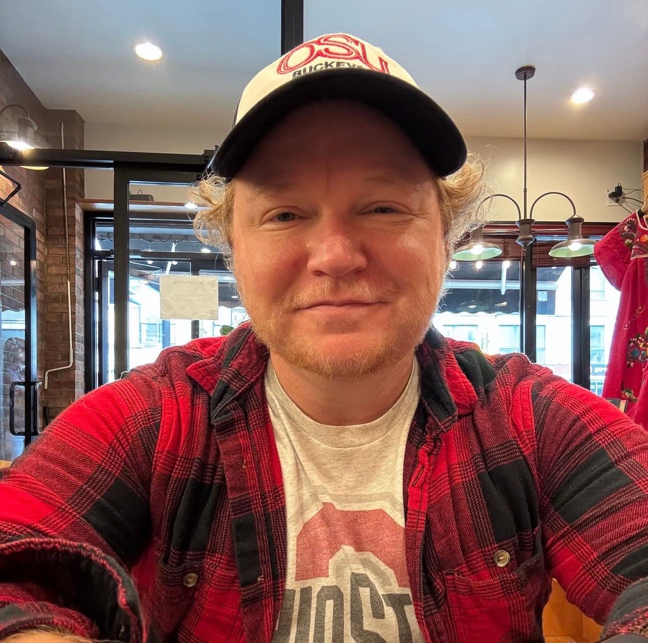 A smiling person wearing an Ohio State cap and plaid shirt in an indoor setting.