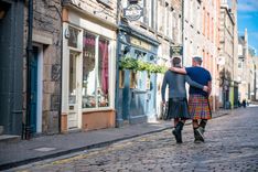 Two men wearing kilts walking arm in arm in a city street