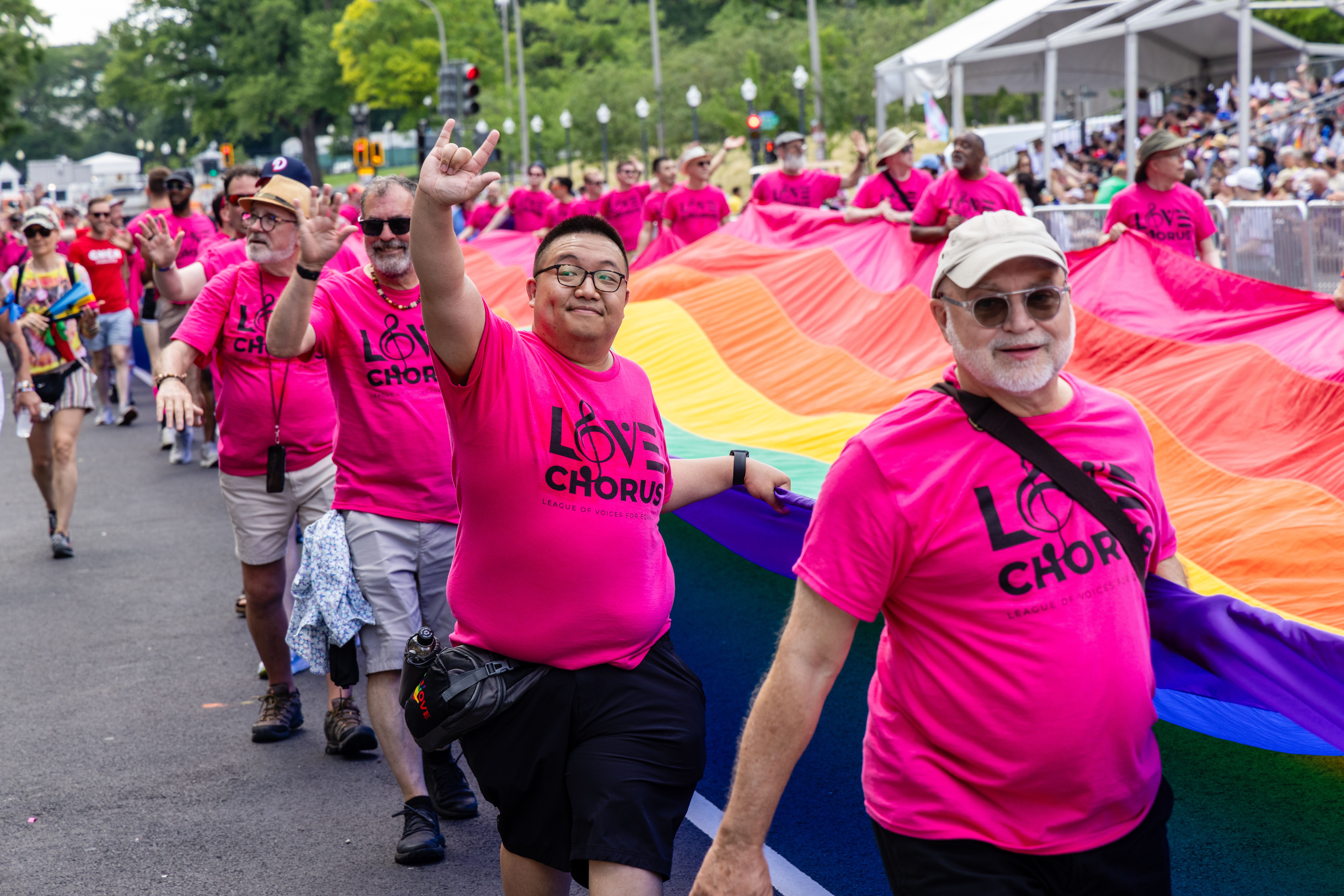 A group of people in pink shirts carrying a large rainbow flag at a lively parade.